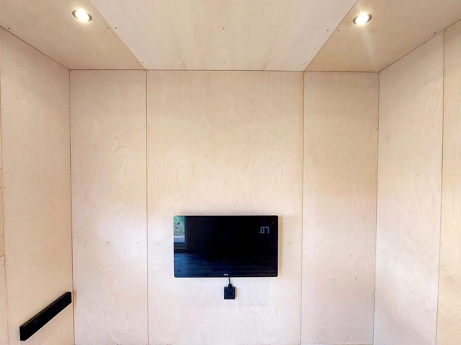 Empty garden room interior lined in birch plywood panels, recessed ceiling downlights