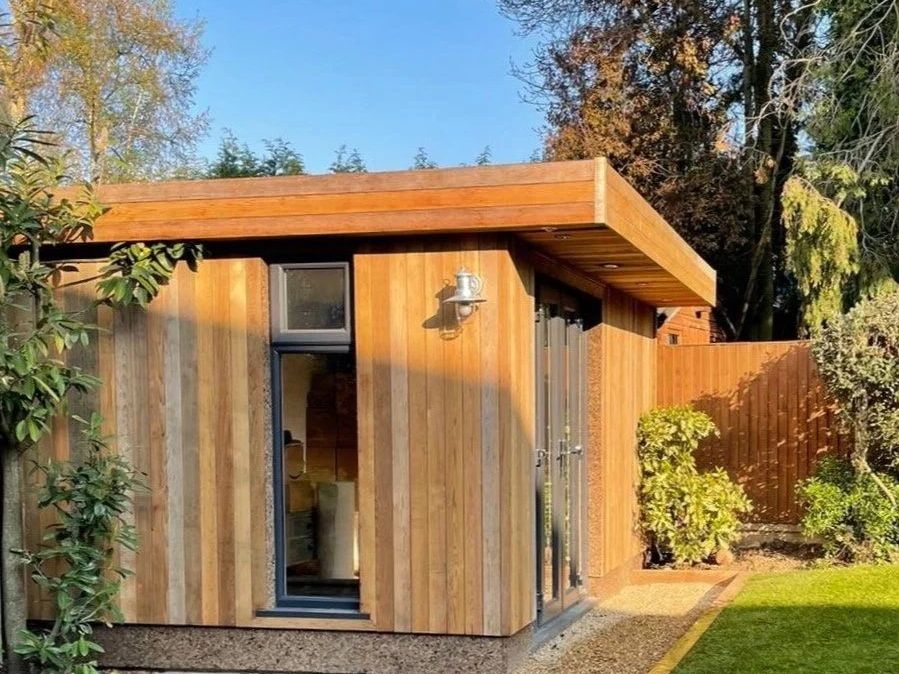 Western red cedar garden office with deep overhanging flat roof, tall slim window and glazed door