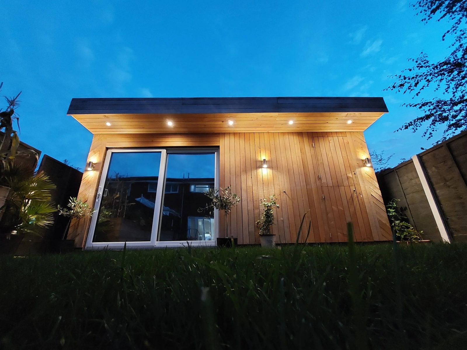 Cedar-clad flat-roof garden studio at dusk, low angle across long grass