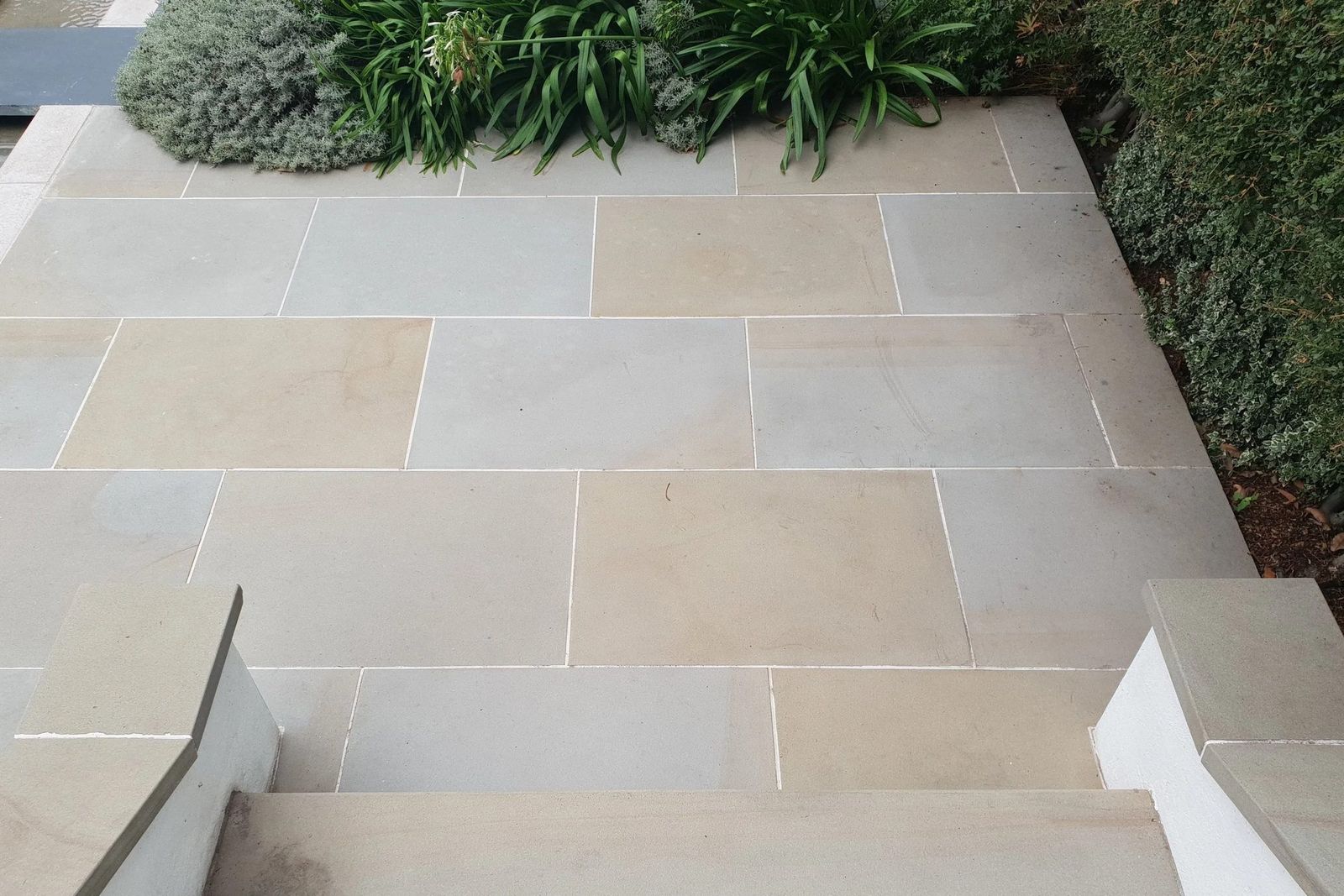 Top-down view of a pale sandstone patio with rendered step and coping stones