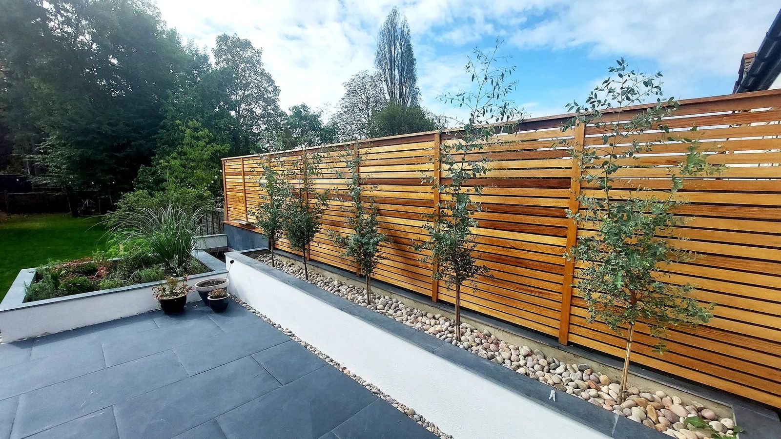 Dark grey slate-paved terrace with white-rendered raised beds, river-pebble border