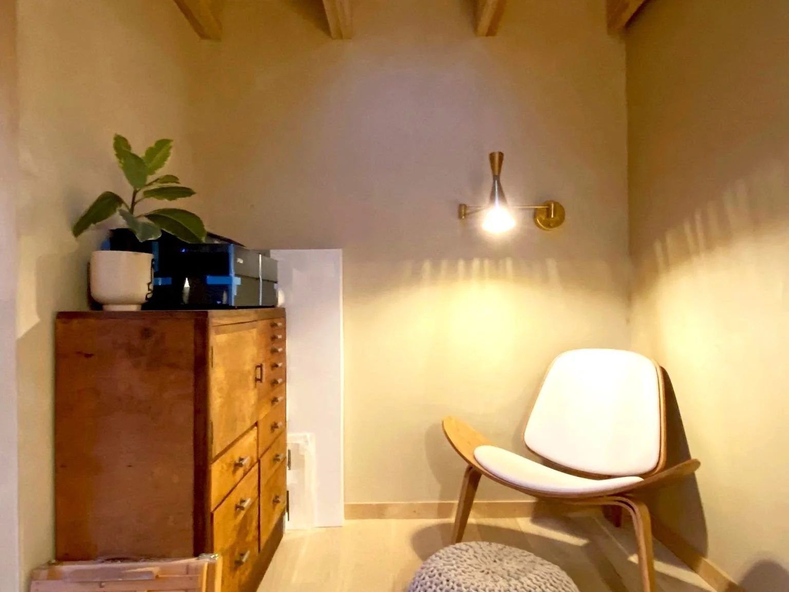 Studio interior corner with rooflight between exposed timber rafters, warm plaster walls, brass wall light