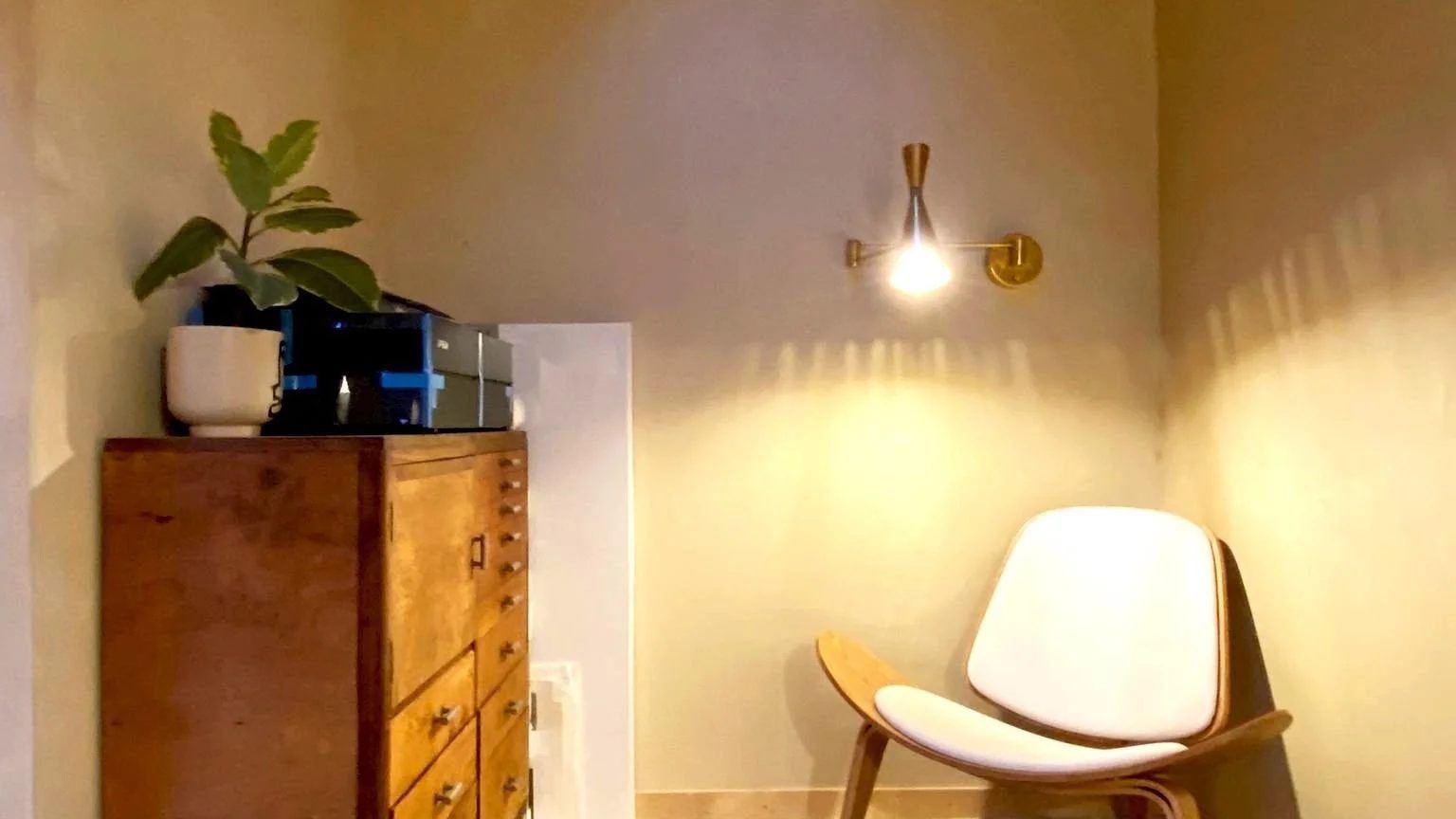 Studio interior corner with rooflight between exposed timber rafters, warm plaster walls, brass wall light