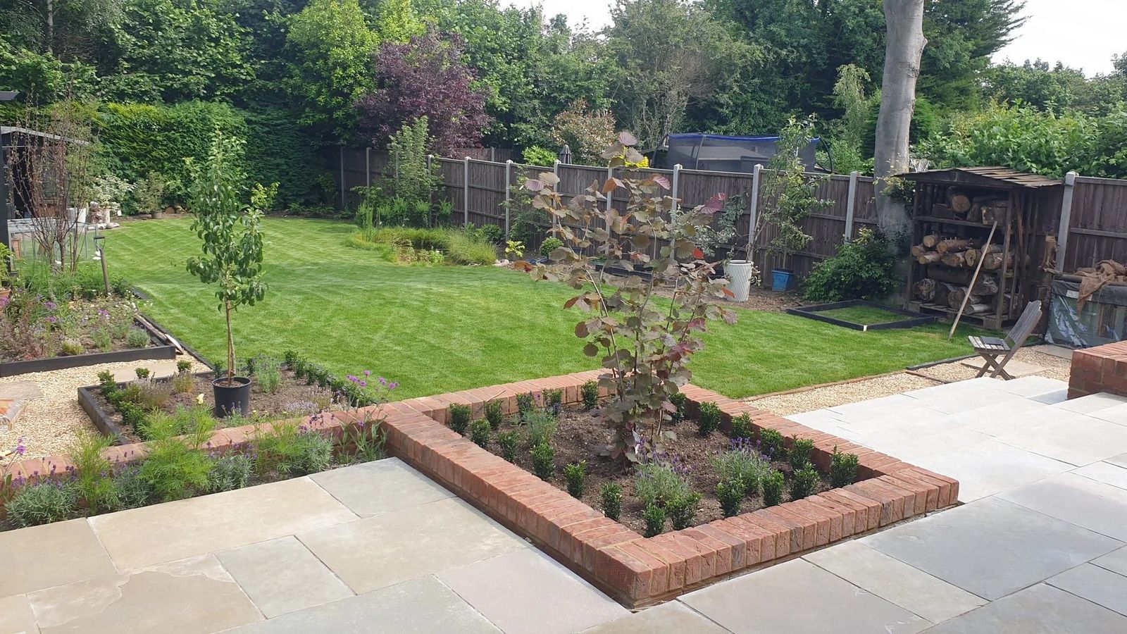 Pale sandstone terrace with red-brick raised planting beds and young trees